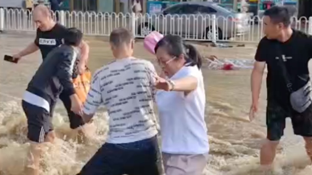 暴雨致道路积水淹到小腿肚，三位小伙自发接力帮助路人通过